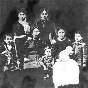 A portrait of a Native American woman in a black dress with seven children of different ages around her. One of them is wearing a cross, and another holds a violin. 