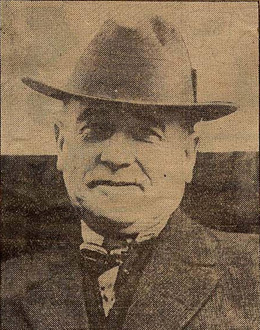 Head and shoulders portrait of a man wearing a large cowboy hat, suit jacket, and tie. 