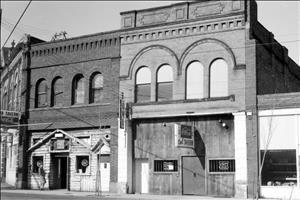 Three two-story brick buildings with dentils, rounded windows and mounted signs reading Tavern and Owl Tavern beneath a Coca-Cola logo