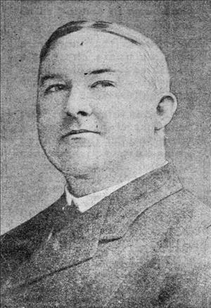 Cort posing in a dark suit with short hair parted down the middle