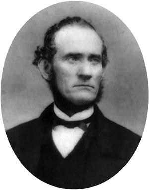 Head and shoulders oval portrait of a man wearing a dark coat, and a bow tie. He has a stern expression on his face, and a chin curtain beard. 